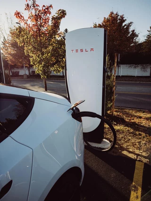 An EV plugged into a Tesla Supercharger at the curb